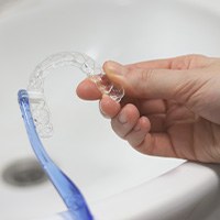 A person cleaning their aligner with toothbrush