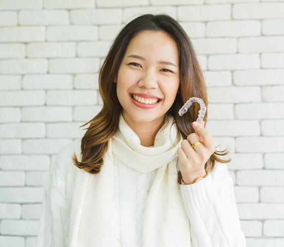 Person holding a clear aligner and smiling in Aurora